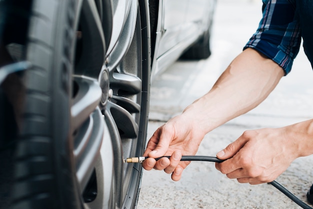 Uomo che per mezzo della pompa di aria sulla ruota di automobile