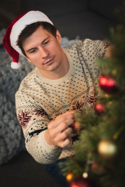 Uomo che porta il cappello di Santa che decora l'albero di Natale