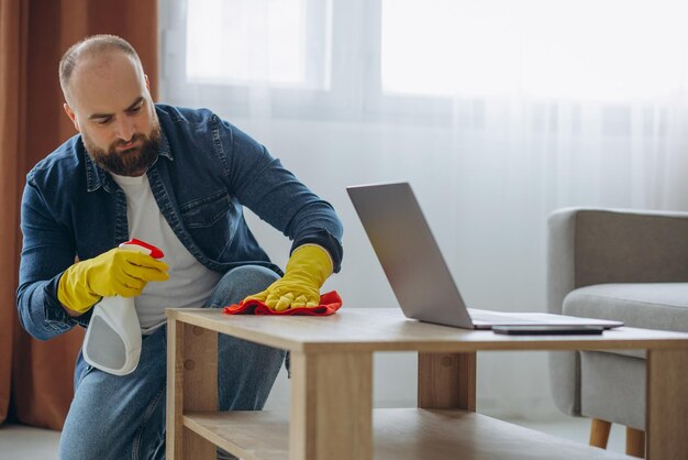 Uomo che pulisce a casa indossando guanti di gomma e usando spray