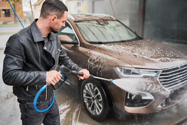 Uomo che pulisce l'auto con l'acqua dalla pistola ad acqua ad alta pressione