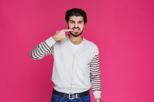 Uomo che punta i denti o la bocca con le dita che significa sorridere o salute orale.