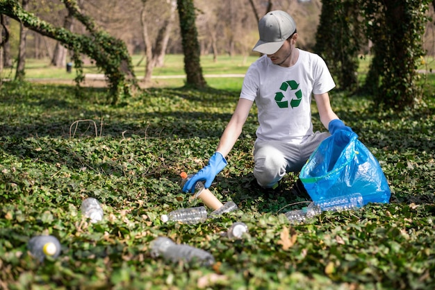 Uomo che raccoglie rifiuti di plastica in un parco inquinato