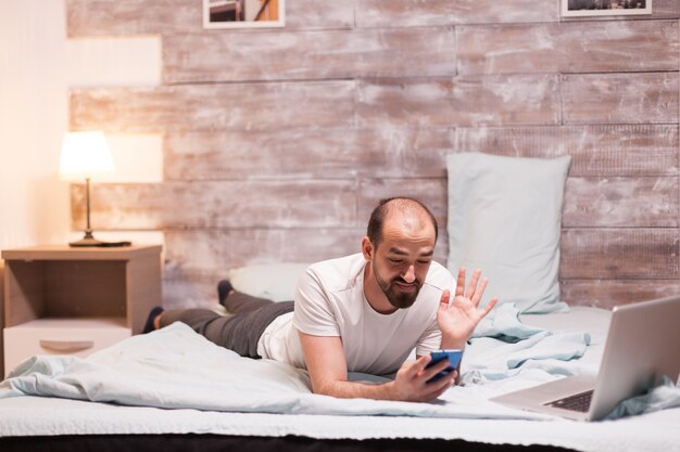 Uomo che riceve una videochiamata a tarda notte mentre si rilassa in camera da letto