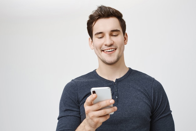 Uomo che ride felice guardando lo schermo del telefono cellulare e sorridente