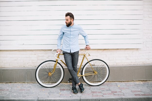 Uomo che si appoggia sulla bicicletta vicino al muro bianco