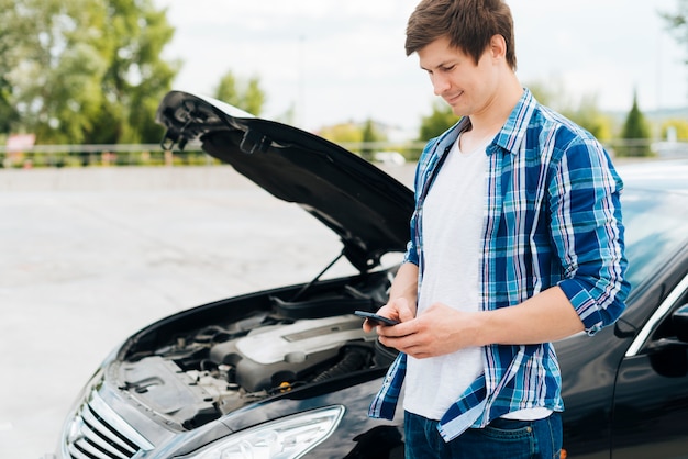 Uomo che si siede sull'automobile e che controlla telefono