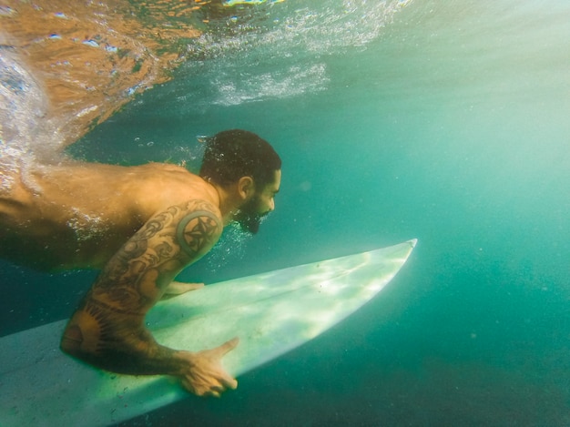 Uomo che si tuffa con la tavola da surf bianca subacquea