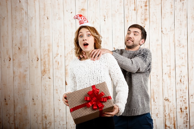 Uomo che soffoca il regalo di natale della tenuta della ragazza sopra la parete di legno