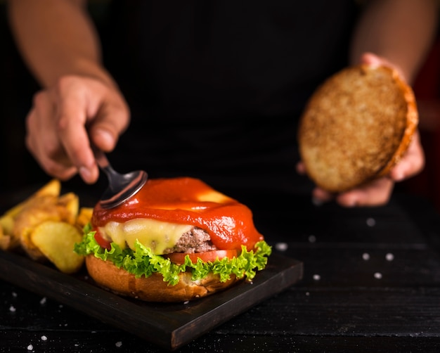 Uomo che sparge ketchup sull'hamburger saporito del manzo