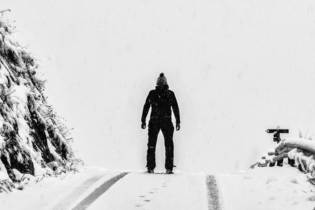 Uomo che sta sul terreno innevato bianco accanto alla montagna