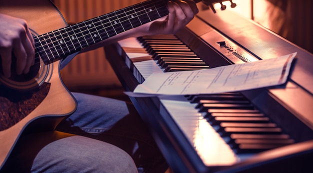 uomo che suona la chitarra acustica e il piano in primo piano, note di registrazione, bel colore di sfondo, concetto di attività musicale