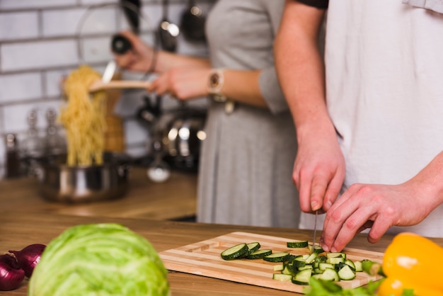 Uomo che taglia cetrioli e donna che cucina la pasta