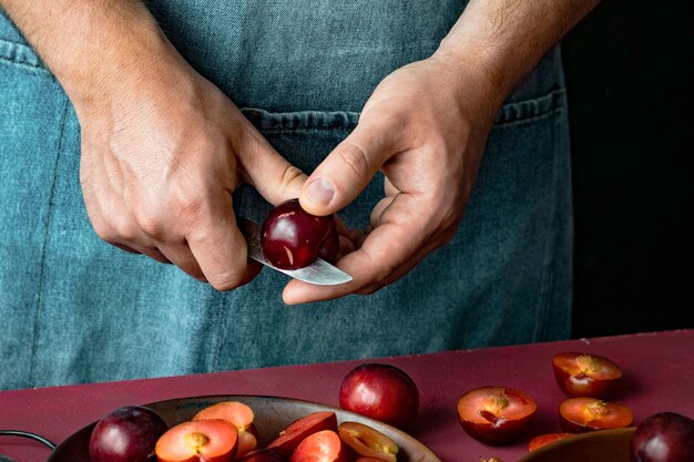 Uomo che taglia le prugne rosse in una cucina