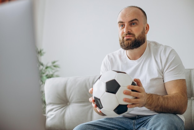 Uomo che tiene il pallone da calcio e guarda il calcio online a casa