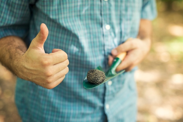 Uomo che tiene il tartufo nero con il pollice in su in natura