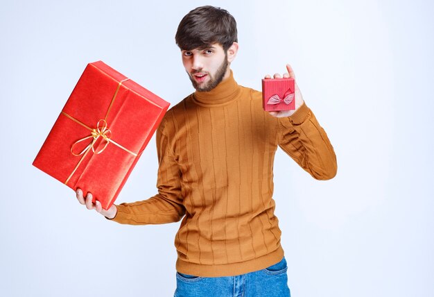 Uomo che tiene in mano scatole regalo rosse grandi e piccole e ne offre una alla sua ragazza.