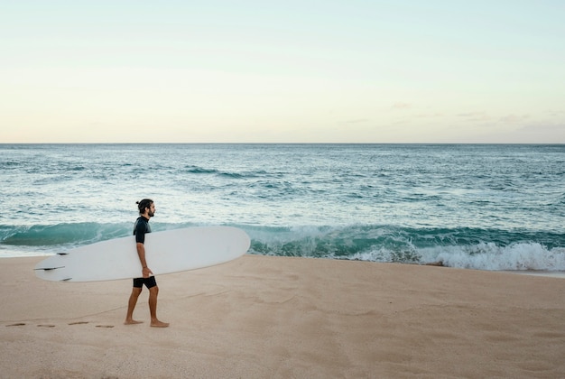 Uomo che tiene la sua tavola da surf vicino all'oceano