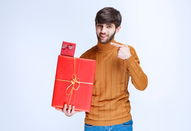 Uomo che tiene scatole regalo rosse grandi e piccole e le dimostra.