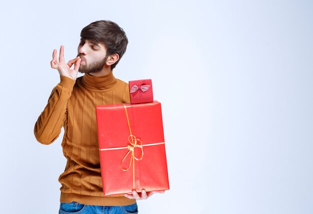 Uomo che tiene scatole regalo rosse grandi e piccole e si diverte.