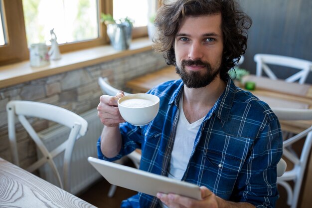 Uomo che tiene tavoletta digitale, pur avendo una tazza di caffè