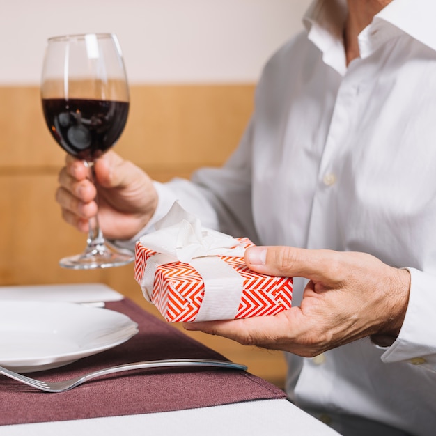 Uomo che tiene un bicchiere di vino e un regalo