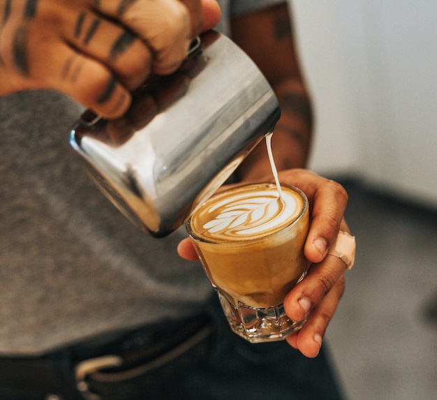 Uomo che tiene un bicchiere trasparente con caffè e versa il latte