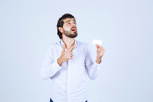 Uomo che tiene un biglietto da visita e indica qualcuno in giro