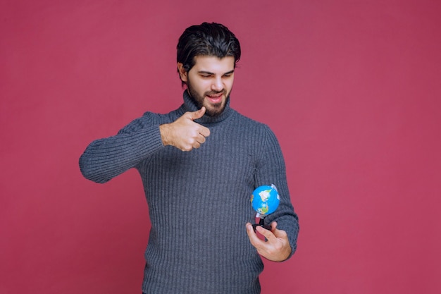 Uomo che tiene un mini globo e che mostra il pollice in su.