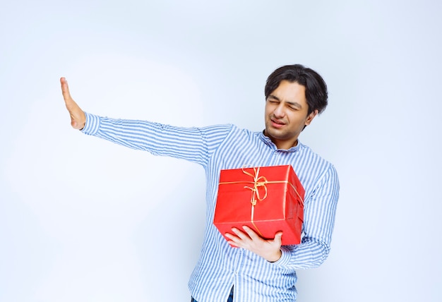 Uomo che tiene una confezione regalo rossa e ferma qualcuno. Foto di alta qualità