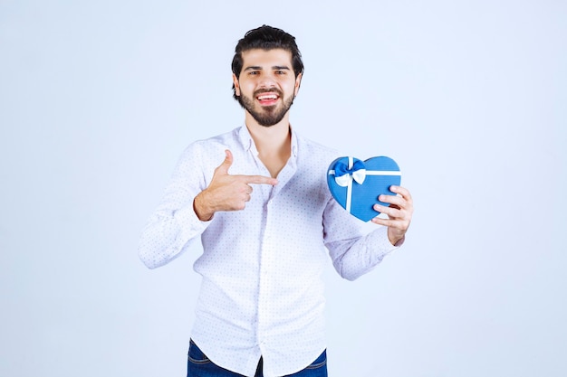 Uomo che tiene una scatola regalo blu a forma di cuore e mostra il pollice in su