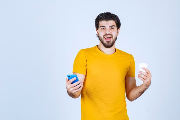 Uomo che tiene una tazza di caffè e che mostra il suo nuovo modello di smartphone.