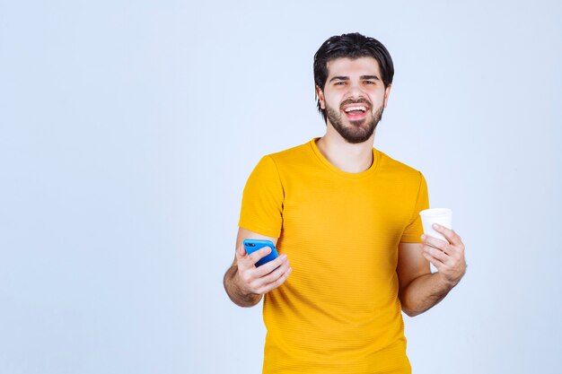 Uomo che tiene una tazza di caffè e che mostra il suo nuovo modello di smartphone.