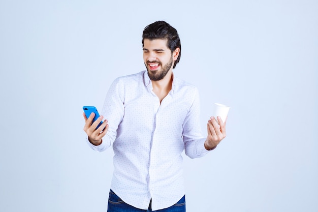 Uomo che tiene una tazza di caffè in una mano e controlla il telefono nell'altra