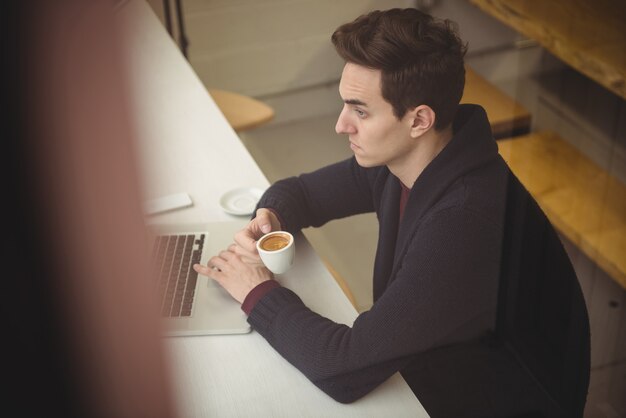 Uomo che utilizza computer portatile mentre beve il caffè