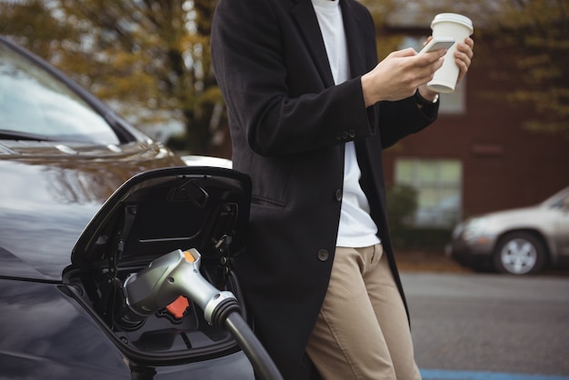 Uomo che utilizza il telefono cellulare durante la ricarica dell'auto