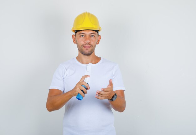 Uomo che utilizza la bottiglia spray per pulire le mani in t-shirt, casco e guardando attento, vista frontale.