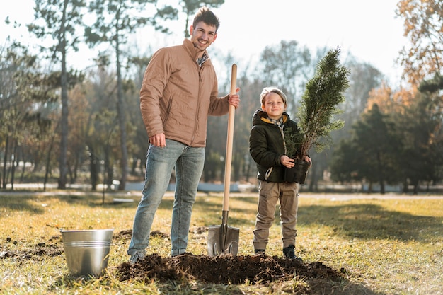 Uomo che utilizza la pala per scavare una buca per piantare un albero mentre posa accanto al figlio