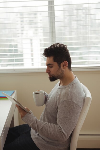 Uomo che utilizza la tavoletta digitale sorseggiando un caffè