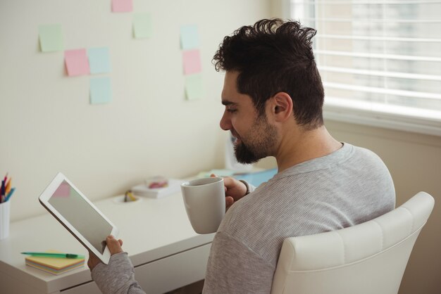 Uomo che utilizza la tavoletta digitale sorseggiando un caffè