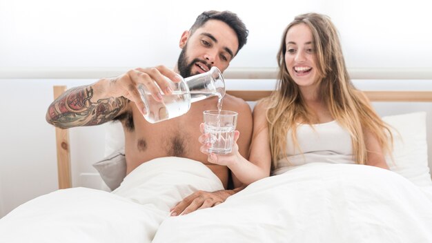 Uomo che versa acqua in vetro per sua moglie in camera da letto