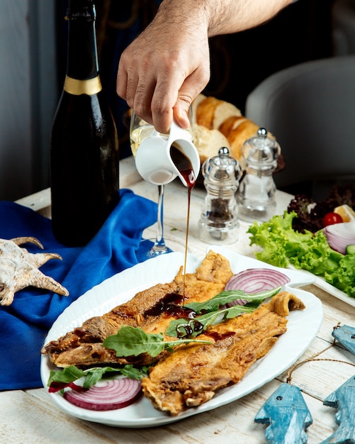 Uomo che versa nar sharab salsa di melograno sul pesce fritto