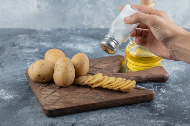 Uomo che versa sale sulle patate a fette. Foto di alta qualità