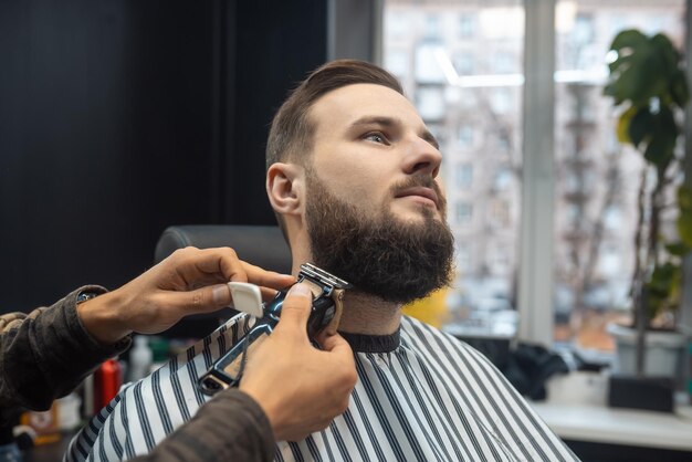 Uomo che visita parrucchiere nel negozio di barbiere. Il barbiere lavora con un tagliacapelli. Cliente hipster che si fa tagliare i capelli.