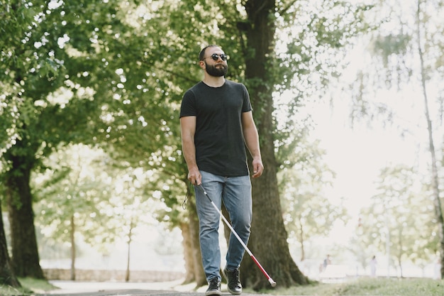 Uomo cieco. Persone con disabilità, portatori di handicap e vita quotidiana. Uomo non vedente con bastone da passeggio, gradini discendenti nel parco cittadino.