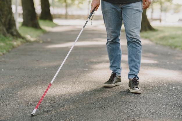 Uomo cieco. Persone con disabilità, portatori di handicap e vita quotidiana. Uomo non vedente con bastone da passeggio, gradini discendenti nel parco cittadino.