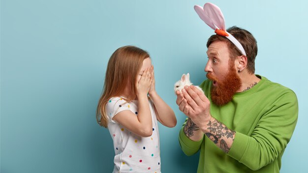 Uomo con barba allo zenzero che indossa abiti colorati e orecchie da coniglio che tiene il coniglietto