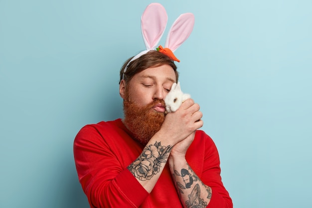 Uomo con barba allo zenzero che indossa abiti colorati e orecchie da coniglio che tiene il coniglietto