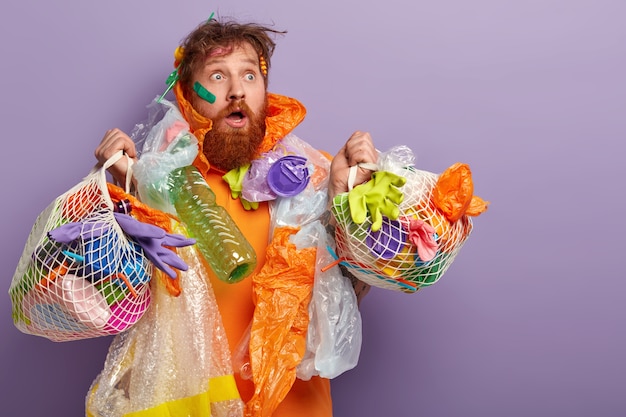 Uomo con barba allo zenzero che tiene i sacchetti con rifiuti di plastica