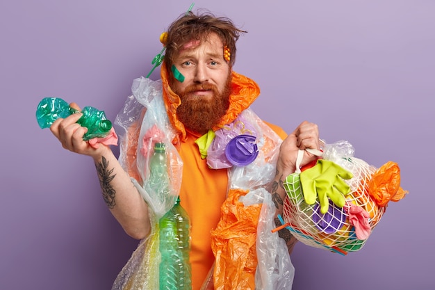 Uomo con barba allo zenzero che tiene i sacchetti con rifiuti di plastica