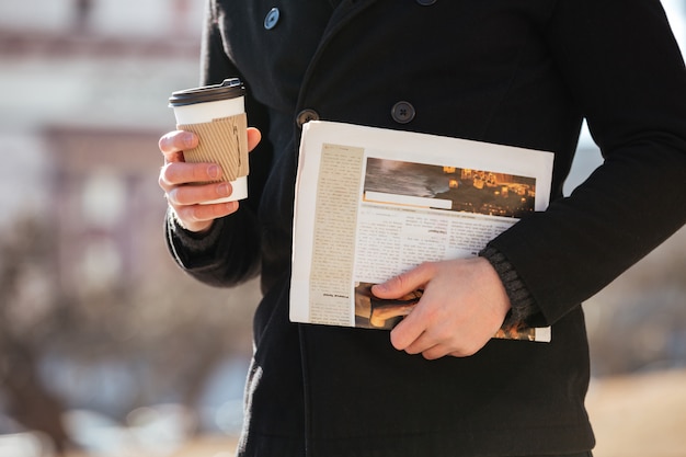 Uomo con caffè e giornale che cammina nella città